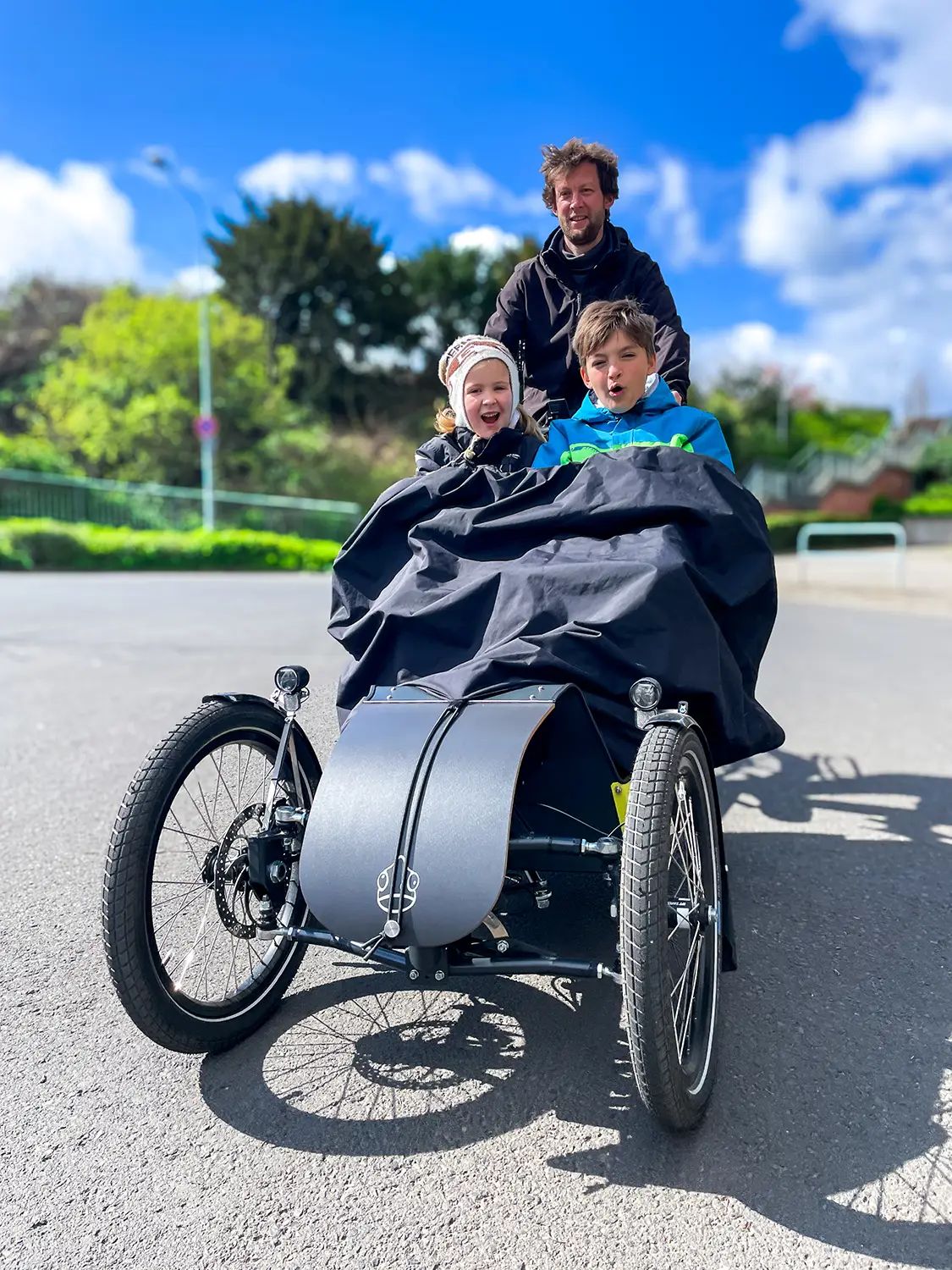 Kinder unter dem Regencape im Lastenrad