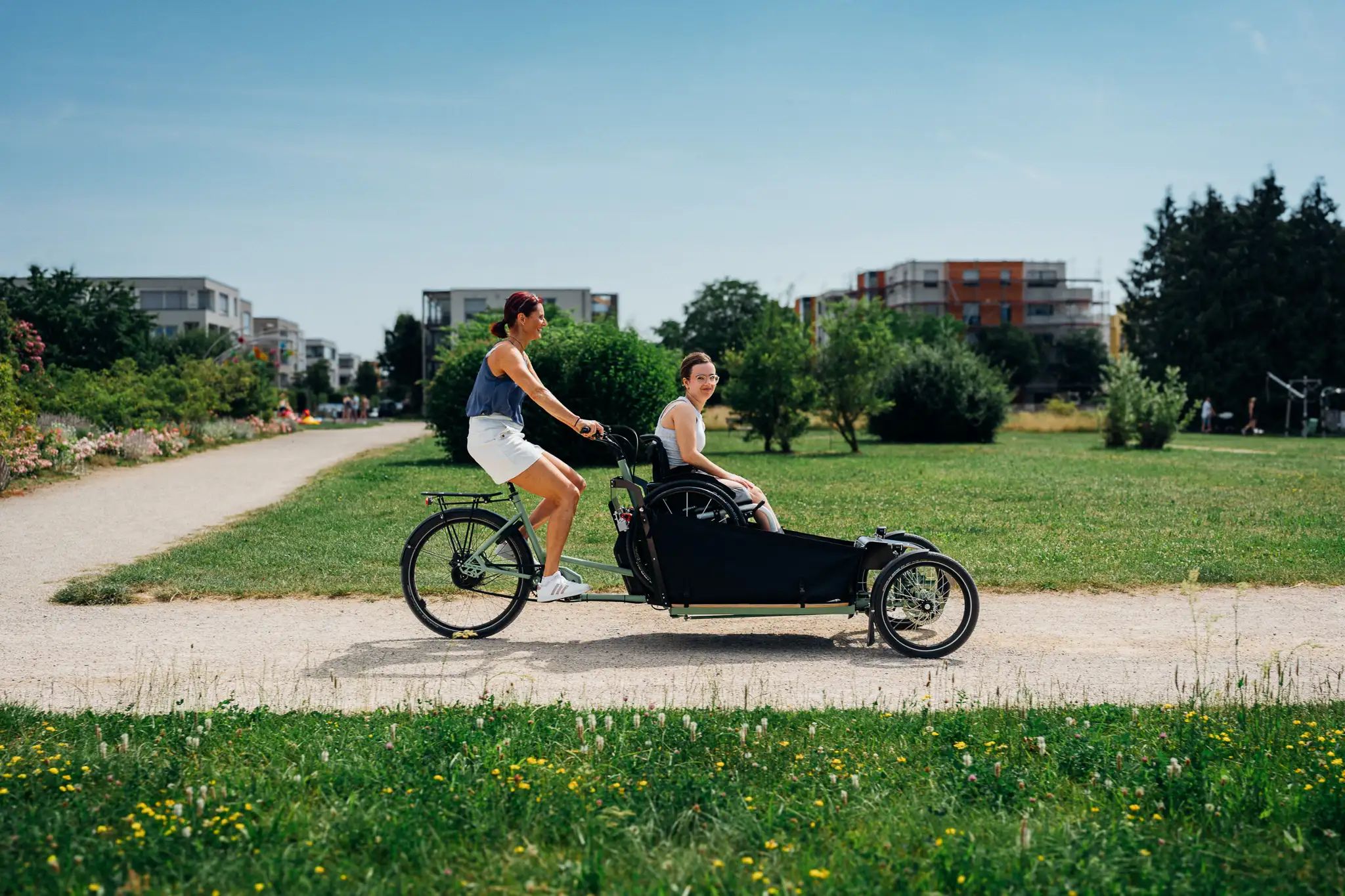 Frau fährt eine Rollstuhlfahrerin im Lastenrad durch einen Park
