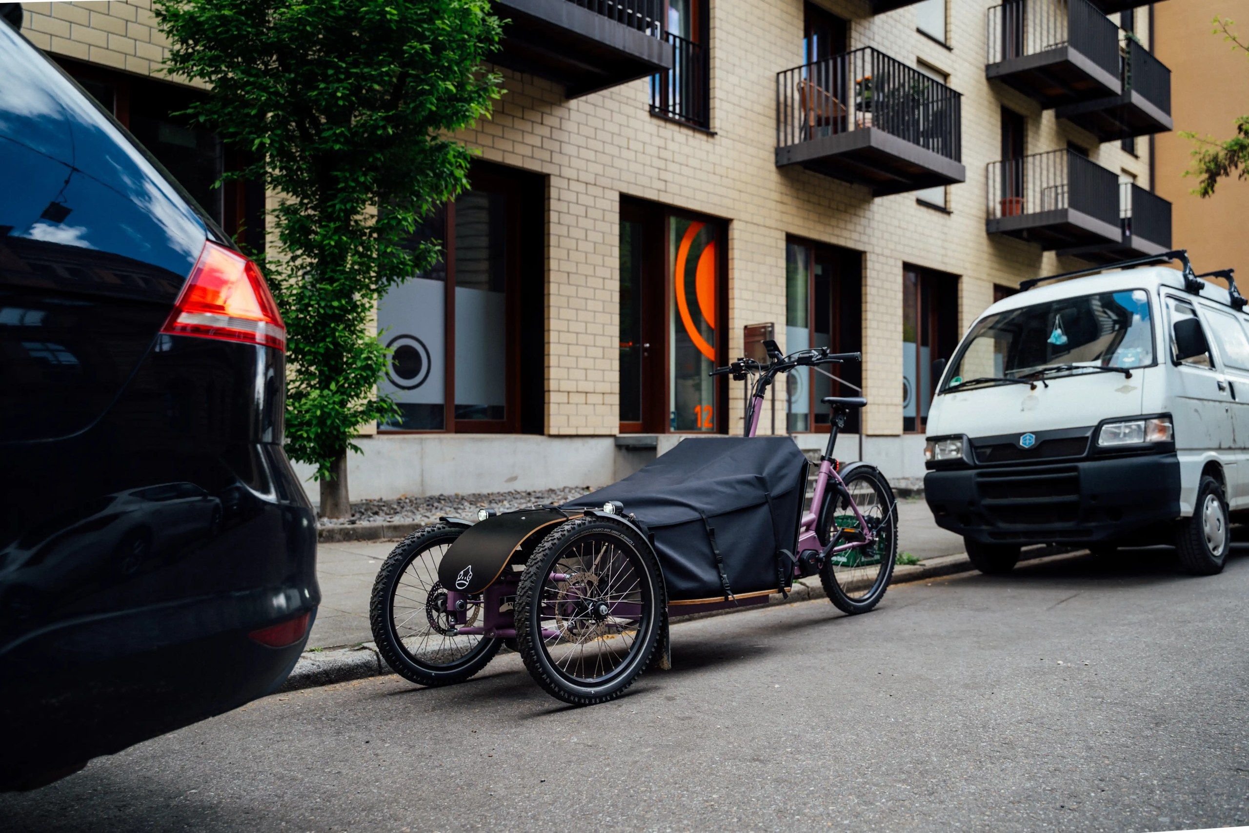 Transporter Bike parkt in einer Stadtstraße zwischen einem Auto und einem Kleintransporter