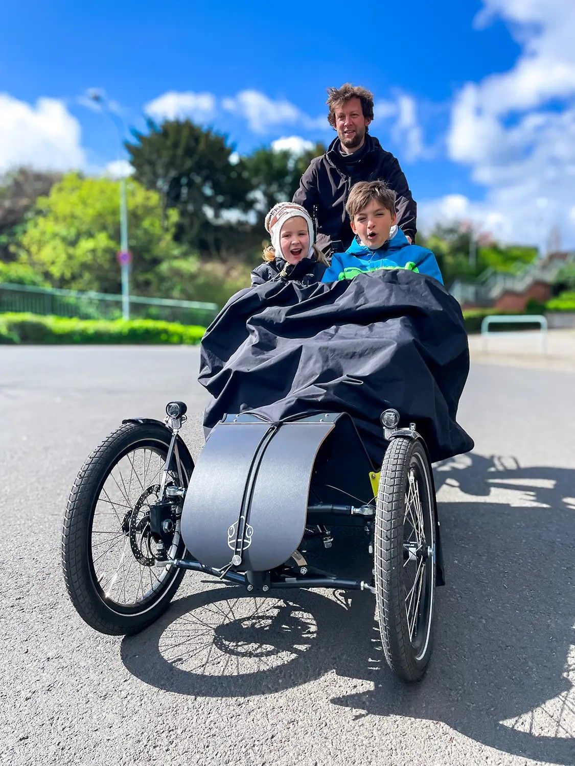 Zwei lachende Kinder unter dem Regencape im Lastenrad